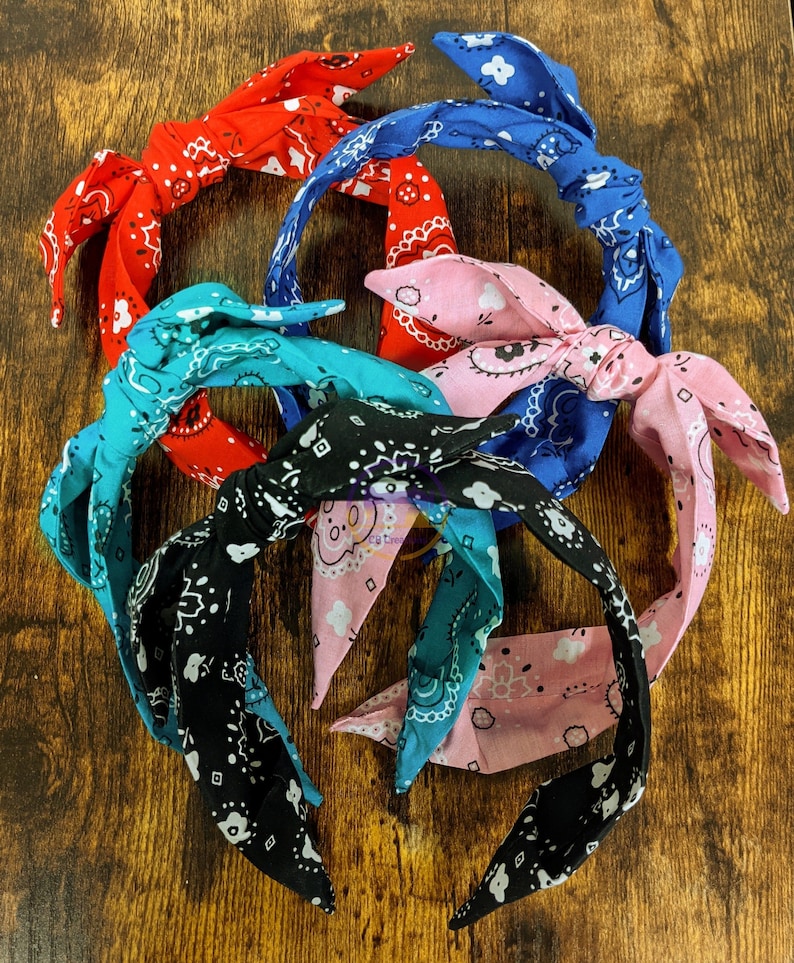 May include: A set of six colorful patterned headbands with a knotted bow detail. The headbands are made of fabric and have a variety of colors and patterns, including blue, red, pink, black, and white.