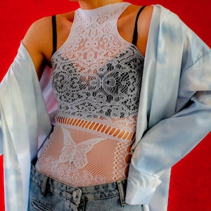 May include: A white lace bodysuit with a butterfly design, worn over a black lace bra. The bodysuit is paired with a light blue shirt and blue jeans.