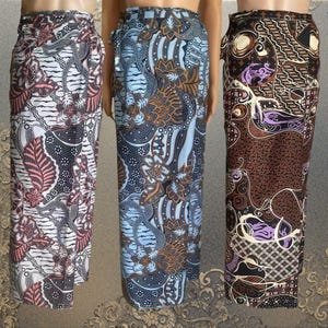 May include: Three wrap skirts featuring intricate batik patterns. The left skirt has a white base with black and pink floral motifs. The center skirt displays a light blue base with dark blue and brown floral designs. The right skirt is black with brown and purple patterns.