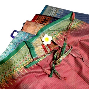 May include: A stack of colorful fabric with a geometric pattern. The fabric is folded and tied together with a green ribbon. A white flower is placed on top of the fabric.