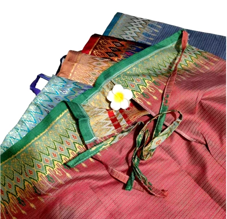 May include: A stack of colorful fabric with a geometric pattern. The fabric is folded and tied together with a green ribbon. A white flower is placed on top of the fabric.