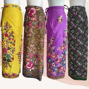 May include: Four wrap skirts displayed on mannequins. The first is yellow with a floral pattern, the second is brown with a dense floral print, the third is purple with scattered floral motifs, and the fourth is dark green with a detailed floral pattern.