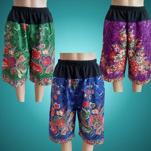 May include: Three pairs of patterned shorts in green, blue, and purple, each with a black waistband. The shorts feature a floral design with red, yellow, and white flowers. The shorts are displayed on mannequin legs.