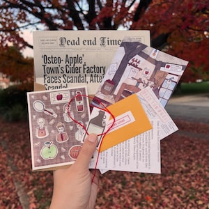 Könnte beinhalten: Eine Sammlung bedruckter Papierartikel, darunter eine Dead End Times-Zeitung, ein Dead End Post-Brief, ein kleiner gelber Umschlag und eine Karte mit Illustrationen von Skeletten, Äpfeln und Apfelweinflaschen, zusammengebunden mit einer roten Schnur.