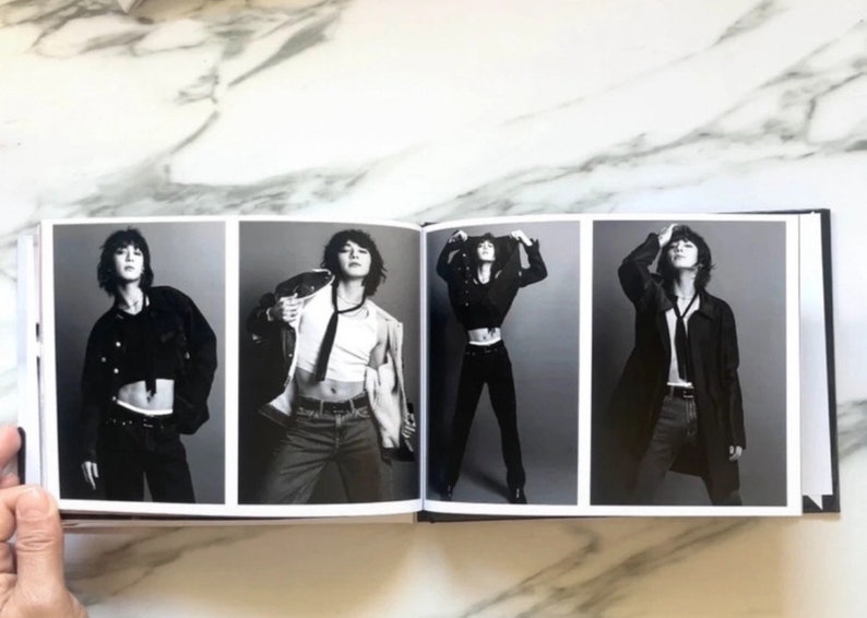 May include: A black and white photo book with four images of a person wearing different outfits. The person is wearing a black crop top, a white tank top, a black jacket, and a black coat.