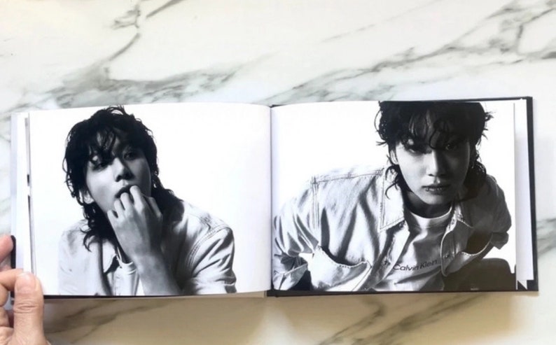May include: A black and white photo of a person wearing a denim jacket with the text "Calvin Klein" on the front. The person is looking at the camera.