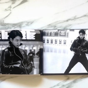 May include: A black and white photo book with two images of a person wearing a black leather jacket. The person on the left is looking to the side, while the person on the right is standing with their legs spread apart.