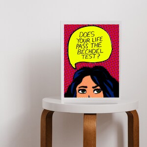 Puede incluir: Una impresi&oacute;n de arte pop enmarcada con el rostro de una mujer y un globo de di&aacute;logo que dice "Does your life pass the Bechdel test?" El fondo es rojo con lunares blancos.