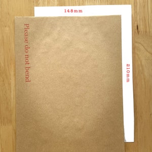 Puede incluir: Un sobre de papel marr&oacute;n con el texto "Please do not bend" impreso en la parte delantera. El sobre mide 148 mm de ancho y 210 mm de alto. El sobre est&aacute; sobre una superficie de madera.