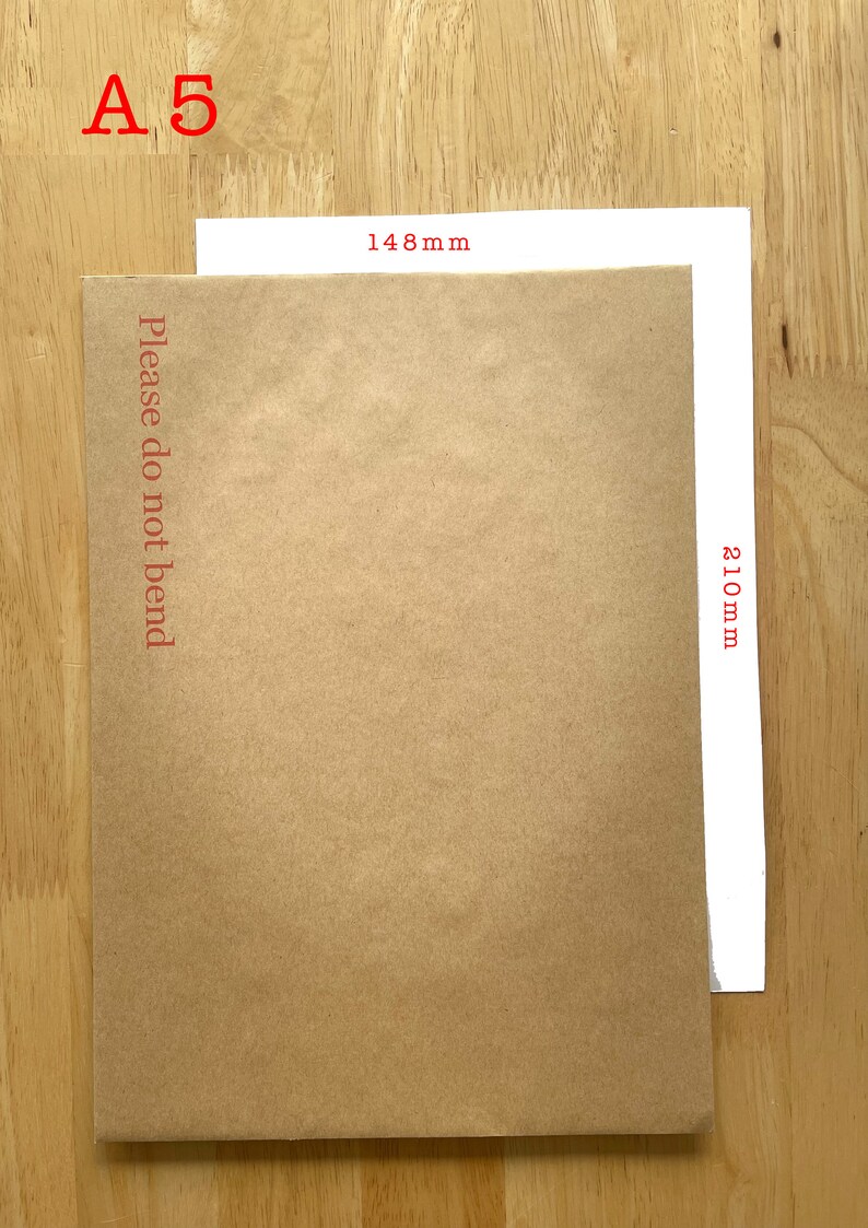 Puede incluir: Un sobre de papel marr&oacute;n con el texto "Please do not bend" impreso en la parte delantera. El sobre mide 148 mm de ancho y 210 mm de alto. El sobre est&aacute; sobre una superficie de madera.