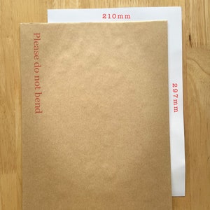 Puede incluir: Un sobre de papel marr&oacute;n con el texto "Please do not bend" impreso en la parte delantera. El sobre mide 210 mm de ancho y 297 mm de largo. El sobre est&aacute; sobre una superficie de madera.