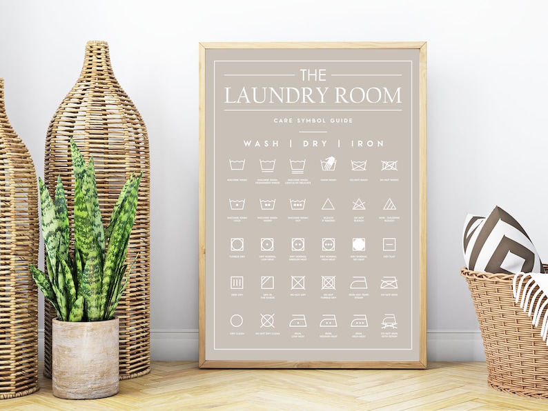 Peut inclure: Une affiche encadr&eacute;e sur fond brun clair avec le texte THE LAUNDRY ROOM CARE SYMBOL GUIDE. L'impression pr&eacute;sente une grille d'ic&ocirc;nes d'entretien du linge blanches class&eacute;es sous les rubriques WASH, DRY et IRON avec des &eacute;tiquettes descriptives.