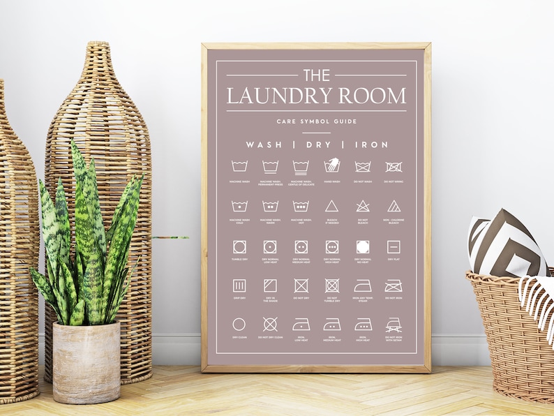 Peut inclure: Une affiche encadr&eacute;e sur fond mauve avec le texte blanc THE LAUNDRY ROOM CARE SYMBOL GUIDE. L'affiche pr&eacute;sente une grille d'ic&ocirc;nes blanches d'entretien du linge class&eacute;es sous les rubriques WASH, DRY et IRON.