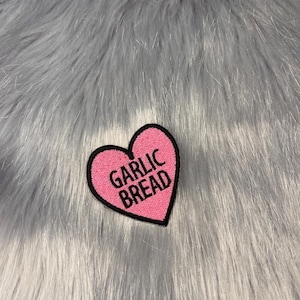 Op de afbeelding: Roze hartvormige patch met de tekst "GARLIC BREAD" in zwarte letters.