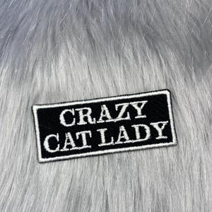 May include: A rectangular black embroidered patch with a white border and the white text CRAZY CAT LADY stitched in a bold serif font. The patch features a clean, high-contrast design with clear lettering and a finished edge.