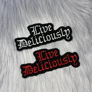 May include: Two embroidered patches featuring the text Live Deliciously in a gothic font. One patch has white lettering on a black background, and the other patch has red lettering on a black background. Both patches have a black border.