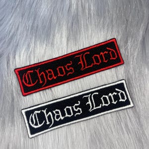 May include: Two rectangular embroidered patches featuring the text "Chaos Lord" in a gothic font. The top patch has red lettering and a red border on a black background. The bottom patch has white lettering and a white border on a black background.