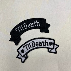 Könnte beinhalten: Zwei gestickte Patches mit dem Text "Til Death" in weißen Buchstaben auf schwarzem und weißem Hintergrund. Der schwarze Patch hat ein einfaches Banner-Design. Der weiße Patch hat ein Banner-Design mit zwei kleinen Herzen.