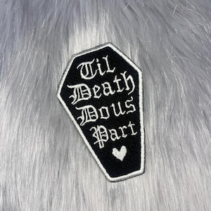 May include: A coffin-shaped embroidered patch with a black background and a white border. The text reads Til Death Dous Part in a white gothic-style font, positioned above a small white embroidered heart at the bottom of the patch.