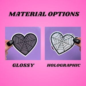 May include: Two heart-shaped stickers with a spiderweb design. The sticker on the left is glossy and the sticker on the right is holographic.