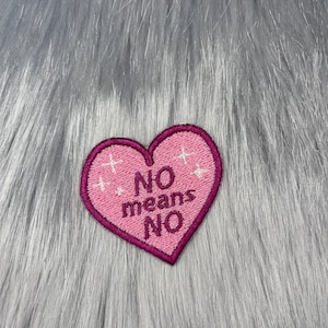 Peut inclure: Patch en forme de cœur rose avec le texte "NO means NO" en lettres blanches. Le patch a un design de paillettes blanches autour des bords.