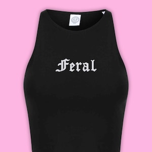 May include: A black sleeveless crop top featuring a high neckline and the word Feral printed in a white gothic-style font across the chest. A white brand label with the letters SF is visible at the inside of the neckline on the collar.