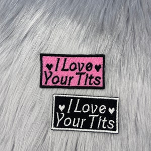 May include: Two rectangular embroidered patches with the phrase "I Love Your Tits". One patch has a pink background with black text and hearts, the other has a black background with white text and hearts.