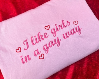 May include: Pink t-shirt with the text "I like girls in a gay way" embroidered in pink with hearts.