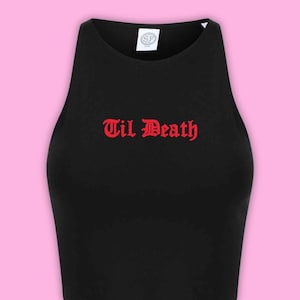May include: A black sleeveless crop top featuring a high neckline and the text "Til Death" printed in a red gothic-style font across the chest. A white brand label with the letters "SF" is visible at the inside of the neckline.