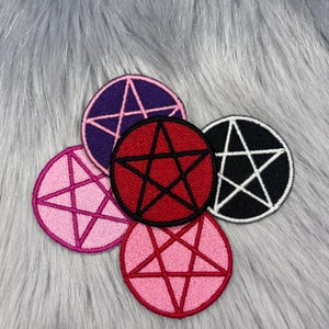 Peut inclure: Cinq patchs pentagrammes brodés de différentes couleurs. Les patchs sont ronds et ont un contour noir. Les couleurs sont le violet, le rouge, le rose, le rose et le noir.