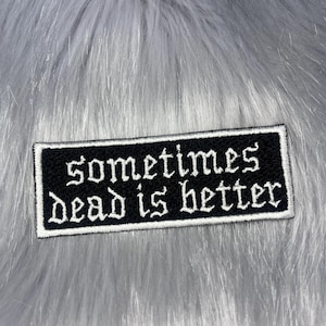 May include: A rectangular embroidered patch with a black background and a white border. The text "sometimes dead is better" is stitched in white using a gothic-style font, centred across two lines on the surface of the patch.