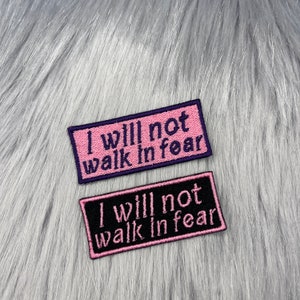 Puede incluir: Dos parches bordados con el texto "I will not walk in fear" en letras rosas sobre un fondo negro y morado.