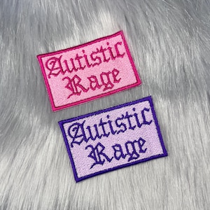May include: Two rectangular embroidered patches featuring the text Autistic Rage in a gothic font. The top patch is pink with dark pink embroidery and a dark pink border. The bottom patch is light purple with dark purple embroidery and a dark purple border.