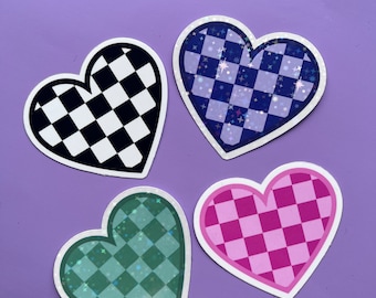 May include: Four heart-shaped stickers with a checkered pattern. The stickers are in black and white, blue and white, pink and white, and green and white. Each sticker has a glittery finish.