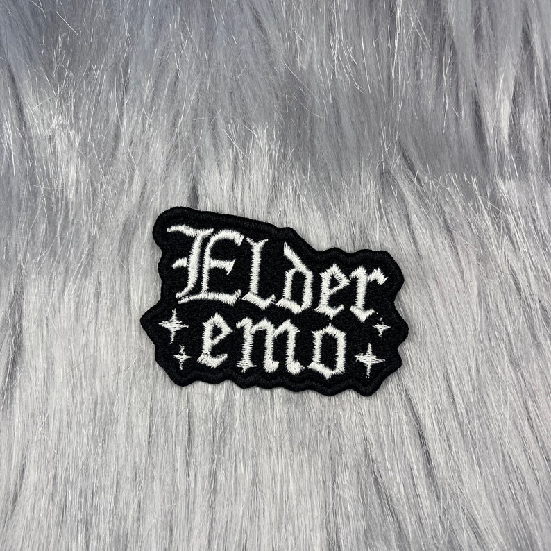 May include: Black embroidered patch with white lettering that reads "Elder emo" with two small white stars on either side.