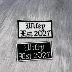 May include: Two rectangular embroidered patches with black and white text. The top patch is white with black text reading Wifey Est 2027. The bottom patch is black with white text reading Wifey Est 2027. Both patches feature a decorative gothic font.