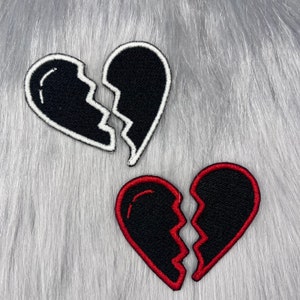 May include: Two embroidered iron-on patches in the shape of broken hearts. One heart is black with white stitching and the other is black with red stitching.