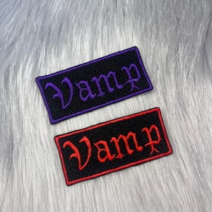 May include: Two rectangular embroidered patches with black backgrounds and borders. One patch features the word Vamp in purple gothic-style lettering, while the other patch features the word Vamp in red gothic-style lettering with a matching red border.