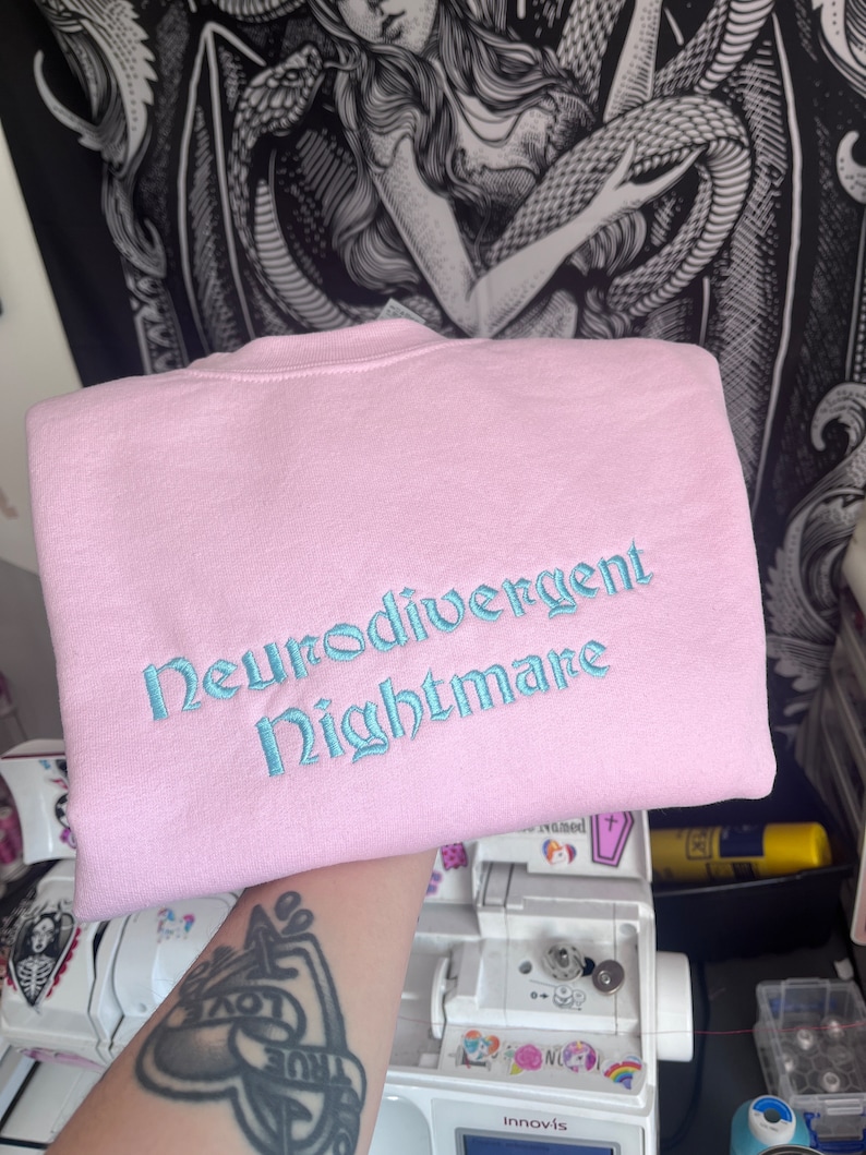 May include: A pink sweatshirt with the text "Neurodivergent Nightmare" embroidered in light blue.