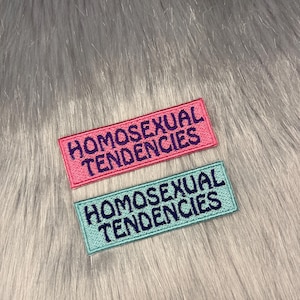 May include: Two embroidered patches with the text "Homosexual Tendencies" in purple lettering. The top patch is pink and the bottom patch is light blue.