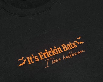 May include: Black sweatshirt with the text "It's Frickin Bats" in orange, with bat graphics, and the phrase "I love halloween" in a cursive font. The sweatshirt is a crew neck style.