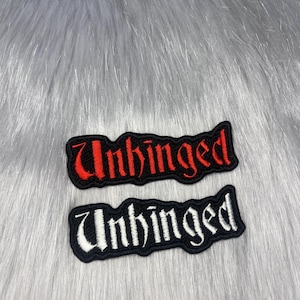 May include: Two black embroidered patches with the word "Unhinged". One patch has red lettering, and the other has white lettering. The patches are on a gray, furry background.