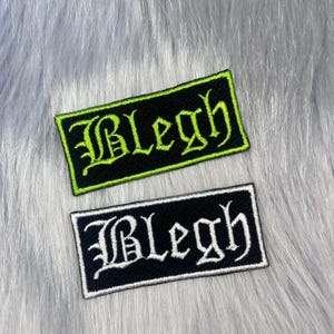 May include: Two rectangular embroidered patches with black backgrounds and borders. The top patch features the text "Blegh" in bright lime green gothic-style lettering. The bottom patch features the same text "Blegh" in white gothic-style lettering.