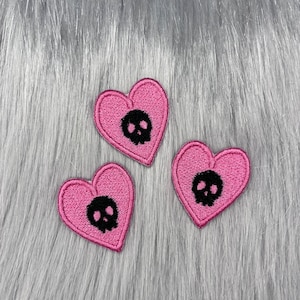 May include: Three pink felt heart-shaped patches with black embroidered skull designs.