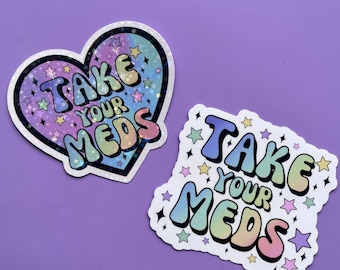May include: Two stickers with the text "Take Your Meds" in rainbow colors with a star pattern. One sticker is a heart shape and the other is a square.
