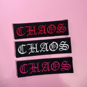 Puede incluir: Tres parches de tela negra con la palabra "CHAOS" bordada en rojo, blanco y rosa.
