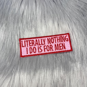 May include: A rectangular embroidered patch with a light pink background and a red border. The text LITERALLY NOTHING I DO IS FOR MEN is stitched in red capital letters across the centre of the patch, which has a visible fabric texture.