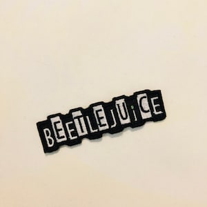 Può includere: Toppa ricamata in bianco e nero con la parola "BEETLEJUICE" in lettere bianche su sfondo nero.