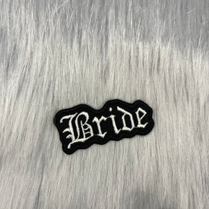 Könnte beinhalten: Schwarzer Stoff-Patch mit weiß gesticktem Schriftzug "Bride" in gotischer Schrift.
