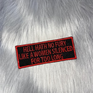 May include: A rectangular embroidered patch with a black background and a red border. The text HELL HATH NO FURY LIKE A WOMEN SILENCED FOR TOO LONG is stitched in red capital letters across the centre of the patch in a simple sans-serif font.